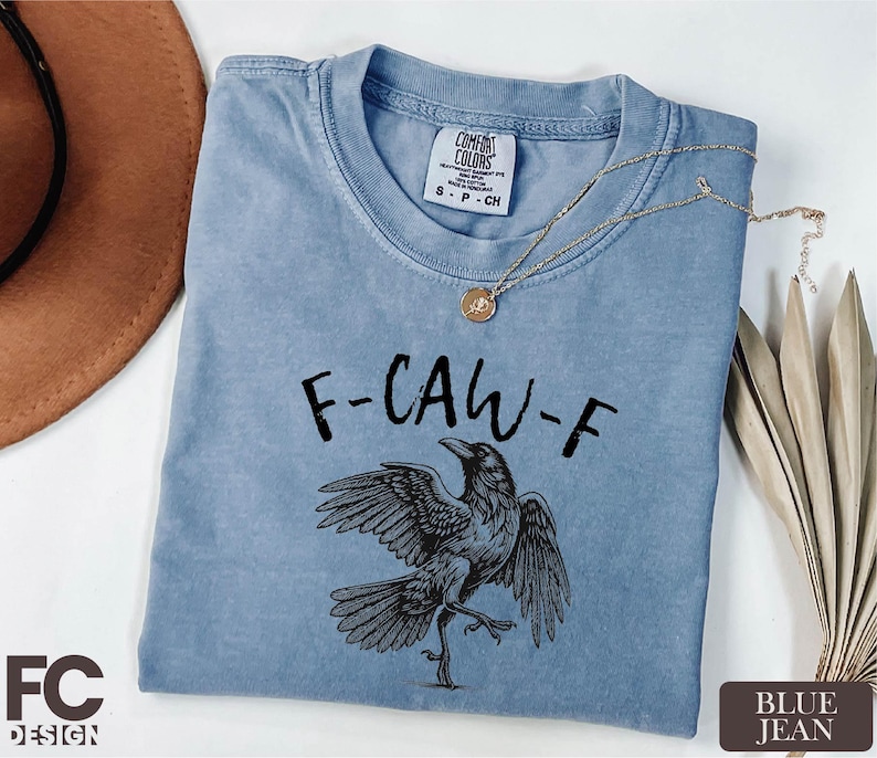 A blue t-shirt with a graphic of a bird and the text "F-CAW-F" printed on it, along with a necklace and a hat.