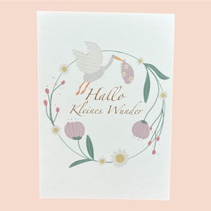 Karte zur Geburt Mädchen – Hallo kleines Wunder | Babykarte mit Storch & Blumenkranz in Rosa | Handgezeichnete Grußkarte auf Kraftpapier