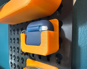 May include: A blue and white case for wireless earbuds is hanging on a black pegboard with orange plastic holders. The pegboard has a grid of holes for hanging items.