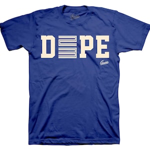 May include: Royal blue t-shirt featuring the word "DOPE" in cream-coloured block letters. The letter "E" is replaced with a cream-coloured graphic of horizontal lines. The shirt has the "Sneakers" logo.