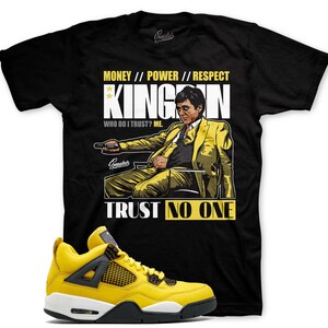 May include: Black t-shirt with a yellow graphic of a man in a suit with the text "MONEY // POWER // RESPECT KINGOON WHO DO I TRUST? ME. TRUST NO ONE". A pair of yellow and black sneakers are in the foreground.