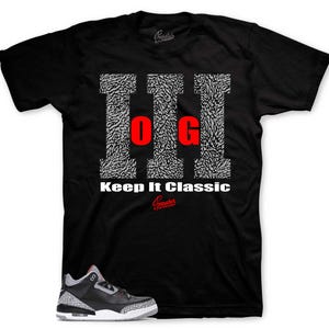 Op de afbeelding: Zwart T-shirt met een witte en grijze olifantprint en de tekst "Keep It Classic". Een paar grijze en zwarte sneakers met rode accenten zijn te zien onder het shirt.