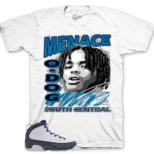 May include: White t-shirt featuring a graphic of a person with the text "MENACE O-DOG SOUTH CENTRAL" in blue. A pair of white and navy blue sneakers are in the foreground.