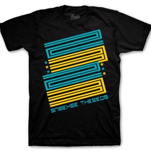 May include: Black t-shirt with a geometric design in teal and yellow. The design includes parallel lines and stars, with the text "SNEAKER THIEVES" in teal below the design. The shirt is a crew neck.