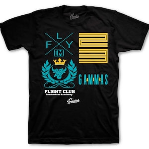 May include: Black t-shirt with multiple graphics in teal and yellow. The graphics include the words "FLY IM", a crown, the words "FLIGHT CLUB Sneakerhead Academy", and the word "GAMMAS".