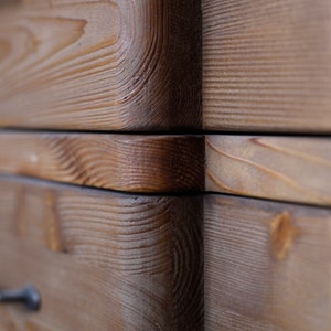 May include: Close-up of a wooden drawer with a natural wood finish. The drawer is made of multiple pieces of wood that are joined together. The wood grain is visible and the drawer has a rustic look.
