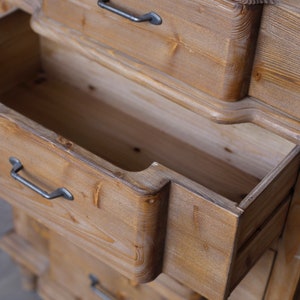 May include: A wooden chest of drawers with multiple drawers. The top drawer is open, revealing the empty interior. The drawers have black metal handles.
