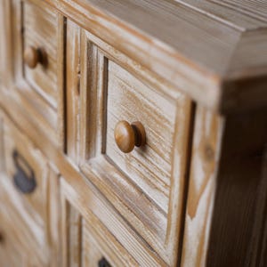 May include: Close-up of a wooden cabinet with multiple drawers. The cabinet has a light brown finish with white accents, and each drawer is adorned with a round, wooden knob. The wood grain is visible, adding texture to the piece.