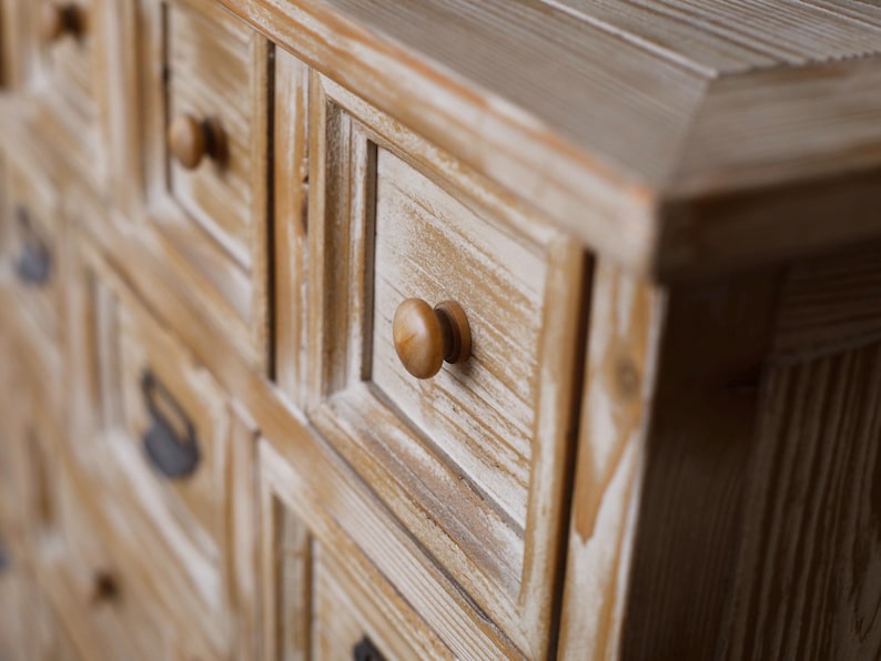 May include: Close-up of a wooden cabinet with multiple drawers. The cabinet has a light brown finish with white accents, and each drawer is adorned with a round, wooden knob. The wood grain is visible, adding texture to the piece.