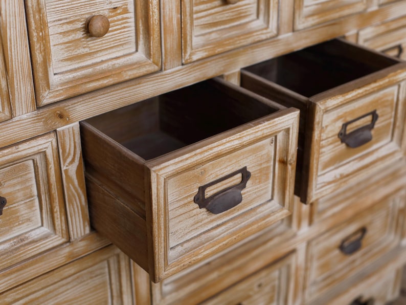 May include: A wooden cabinet with multiple drawers, some open. The cabinet has a light brown, distressed finish. The open drawers reveal a dark interior. Each drawer has a metal handle. The cabinet is made of wood.