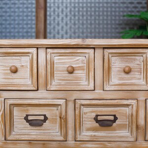 May include: A light brown wooden cabinet with multiple square drawers. The drawers have wooden knobs and metal label holders. The cabinet has a rustic, weathered appearance, with visible wood grain.