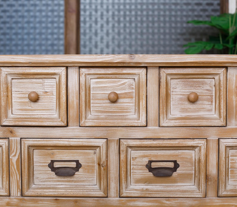May include: A light brown wooden cabinet with multiple square drawers. The drawers have wooden knobs and metal label holders. The cabinet has a rustic, weathered appearance, with visible wood grain.