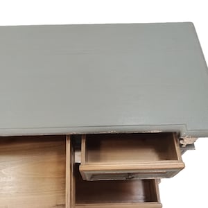 May include: A distressed, light gray painted wooden desk with three drawers. The top of the desk is a solid color, while the drawers are a natural wood tone. One drawer is partially open, revealing the interior.