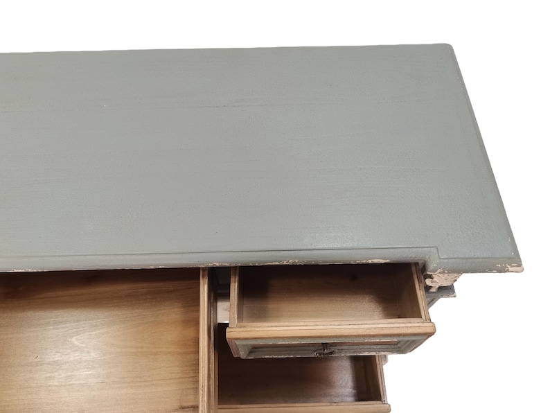 May include: A distressed, light gray painted wooden desk with three drawers. The top of the desk is a solid color, while the drawers are a natural wood tone. One drawer is partially open, revealing the interior.