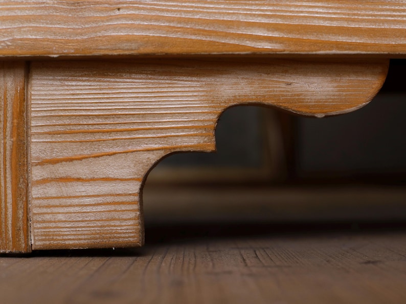 May include: Close-up of a wooden furniture corner joint. The wood has a warm, light brown tone with visible grain patterns. The design includes a decorative, curved cutout detail, adding visual interest to the structure.