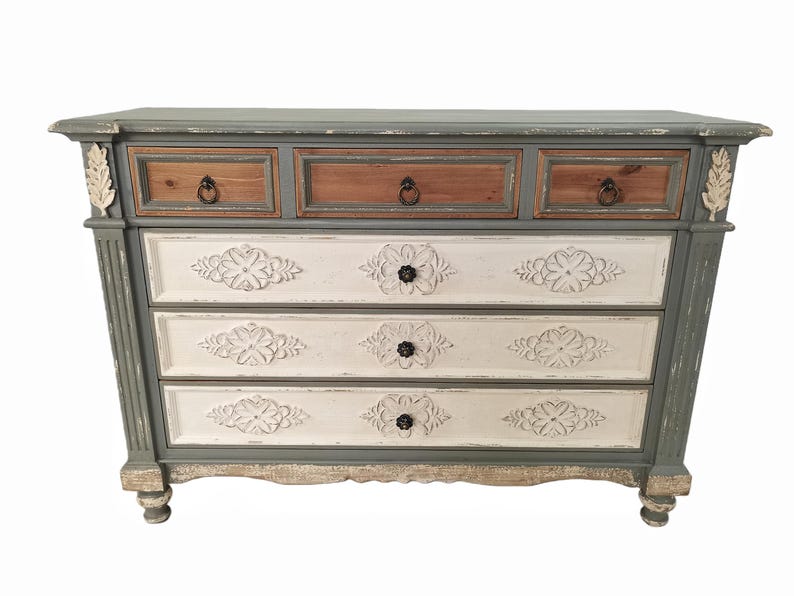 May include: A distressed-finish chest of drawers with three small top drawers and three larger drawers below. The top drawers are brown, the middle drawers are white with floral carvings, and the frame is gray. The chest has decorative accents and ring pulls.