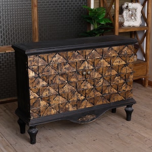 May include: A black wooden cabinet with two doors. The doors are decorated with a geometric pattern of gold-painted triangles. The cabinet has four legs and a decorative trim around the bottom.