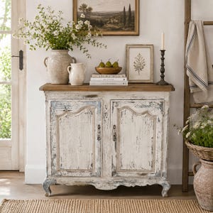Puede incluir: Un aparador blanco y azul desgastado con una tapa de madera, adornado con objetos decorativos. Un jarrón grande con flores, una jarra blanca pequeña y un cuenco de peras descansan encima. También se ven un cuadro enmarcado y un candelabro.