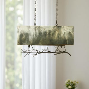 May include: A rectangular pendant light fixture with a textured, abstract design in shades of green, white, and gray. The light hangs from chains and features a decorative branch element. The fixture is suspended in front of a window.