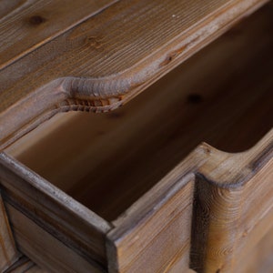 May include: Close-up of a wooden drawer with a carved edge. The drawer is open and the inside is empty.