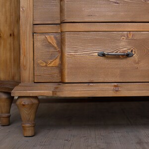 May include: A wooden chest of drawers with four drawers and turned legs. The dresser is made of light brown wood with a natural finish. The drawers have black metal handles.