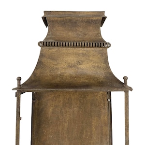May include: A close-up of a bronze-colored lantern with a pagoda-style top. The lantern has a rectangular body and a decorative, curved roof. The metal has a textured, aged appearance, with small decorative finials on the corners.