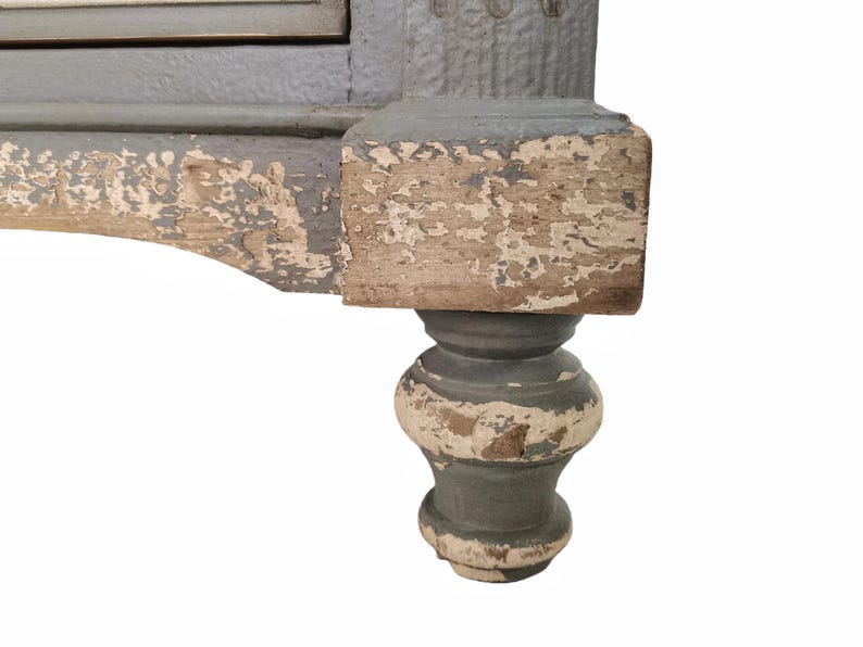 May include: Close-up of a distressed, antique furniture leg. The leg features a turned design with a gray-blue paint finish, showing signs of wear and chipping, revealing the natural wood underneath. The base is a bulbous shape.