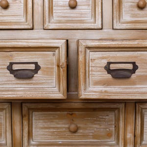 May include: Close-up of a wooden cabinet with multiple drawers. The drawers are framed and have dark metal handles and wooden knobs. The wood has a light, distressed finish, giving it a rustic appearance.