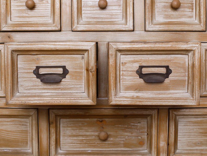 May include: Close-up of a wooden cabinet with multiple drawers. The drawers are framed and have dark metal handles and wooden knobs. The wood has a light, distressed finish, giving it a rustic appearance.