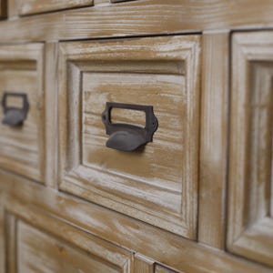 May include: Close-up of a wooden cabinet with multiple drawers. The drawers are a light brown colour with a distressed finish. Each drawer has a dark metal handle. The cabinet appears to be vintage or antique.