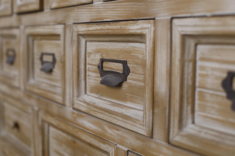 May include: Close-up of a wooden cabinet with multiple drawers. The drawers are a light brown colour with a distressed finish. Each drawer has a dark metal handle. The cabinet appears to be vintage or antique.