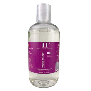May include: A clear plastic bottle of shampoo with a purple label. The label says "Huma in the Kitchen" and "Magical Shampoo" with a 0% dye and fragrance claim. The bottle is 250 ml or 8.4 fl oz.