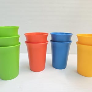 May include: A collection of colorful plastic cups in green, red, blue, and yellow. Each cup has a flared rim and a slightly tapered body. The cups are stacked in pairs, showcasing their vibrant hues.