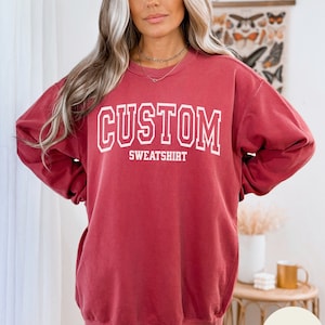 May include: Crimson red oversized sweatshirt with the text "CUSTOM SWEATSHIRT" in white.