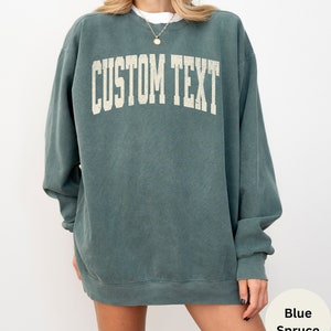May include: A blue spruce colored sweatshirt with the text "CUSTOM TEXT" in a vintage white font.