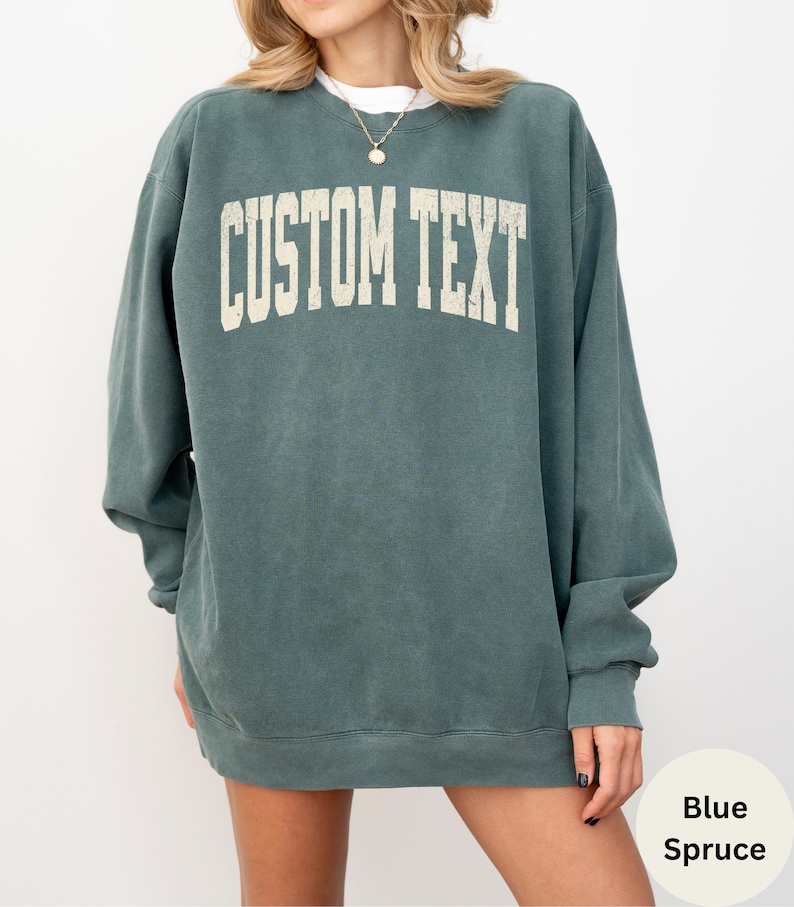 May include: A blue spruce colored sweatshirt with the text "CUSTOM TEXT" in a vintage white font.