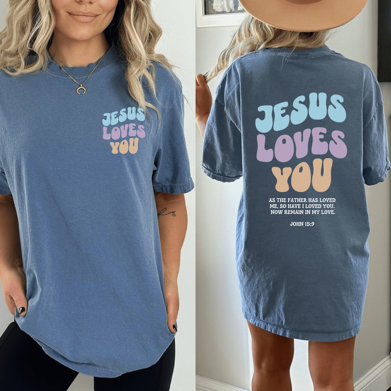 May include: A blue t-shirt with the text "Jesus Loves You" in colorful, retro-style lettering. The back of the shirt has the same text with a Bible verse from John 15:9.
