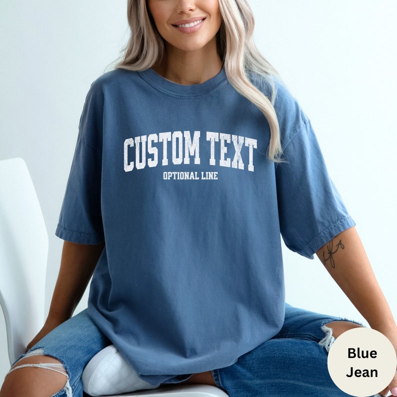 May include: A blue oversized t-shirt with the text "CUSTOM TEXT" and "OPTIONAL LINE" in white. The shirt is made of a soft, comfortable material.
