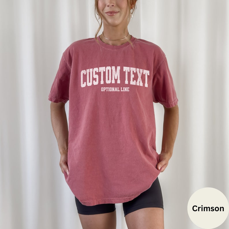 May include: Crimson red oversized t-shirt with white text that reads "CUSTOM TEXT" and "OPTIONAL LINE".