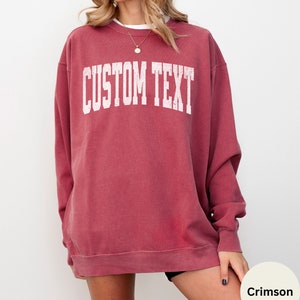 May include: Crimson red sweatshirt with a white distressed graphic that says "CUSTOM TEXT".