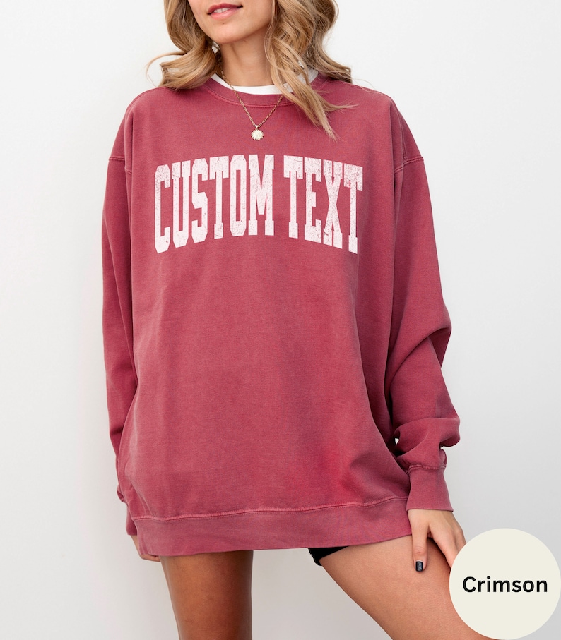 May include: Crimson red sweatshirt with a white distressed graphic that says "CUSTOM TEXT".