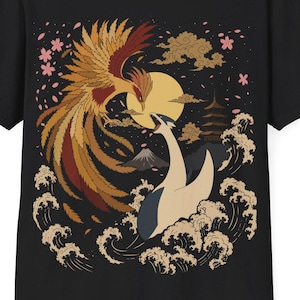 May include: A black short-sleeve t-shirt featuring a graphic print of a golden phoenix and a white crane facing each other over stylized waves. The design includes a yellow sun, a pagoda, a mountain, and pink cherry blossoms on a dark background.