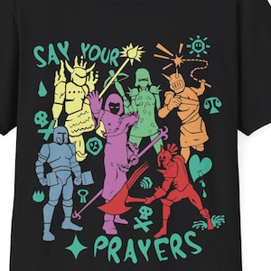 May include: Black t-shirt featuring a colourful graphic of characters and the text "Say Your Prayers".