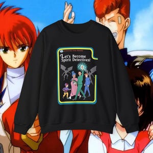 Peut inclure: Sweat-shirt noir à col rond avec un graphisme coloré affichant le texte "Let's Become Spirit Detectives!" et des personnages de dessins animés. Le motif est encadré d'une bordure jaune et bleue. L'arrière-plan présente des personnages d'anime.