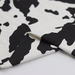 May include: Close-up of white fabric with a black cow print pattern. The fabric is folded over, showing the texture of the material.