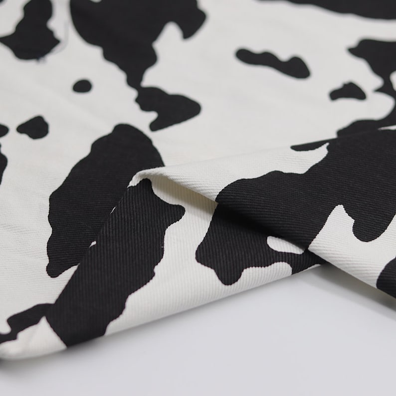 May include: Close-up of white fabric with a black cow print pattern. The fabric is folded over, showing the texture of the material.