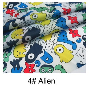 May include: White fabric with a colourful print of cartoon aliens, stars, and words. The fabric is folded in half, showing the pattern on both sides. The text on the fabric says "4# Alien".