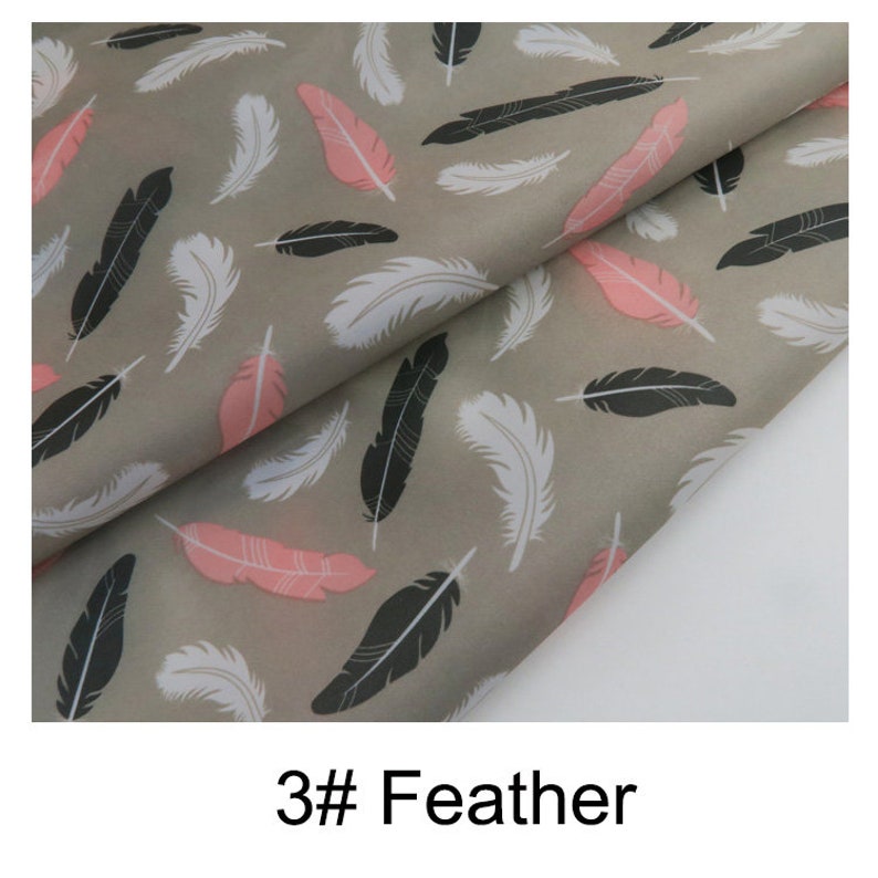 May include: A close-up of a grey fabric with a repeating pattern of pink, white and black feathers. The fabric is folded in half, and the pattern is visible on both sides. The text "3# Feather" is printed below the fabric.