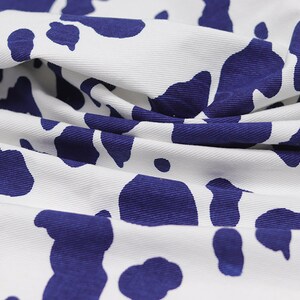 May include: White fabric with a blue cow print pattern. The fabric is folded and wrinkled.