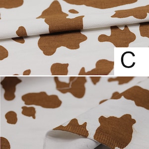 May include: Close-up of white fabric with brown cow print. The fabric has a textured, corduroy-like surface. The letter "C" is visible in the upper right corner of the image.